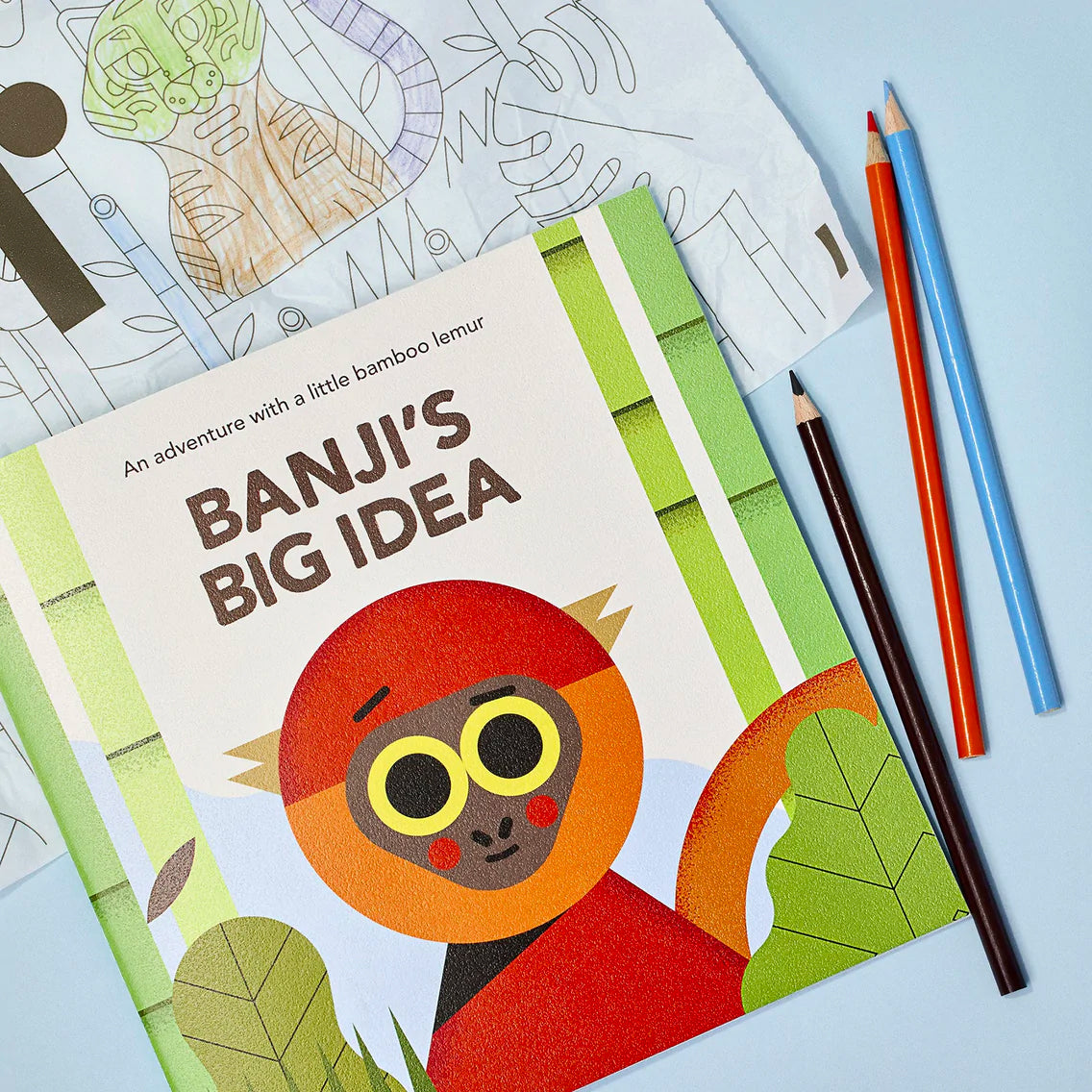 Banji's Big Idea story book next to a coloring page featuring a tiger in a bamboo forest and three color pencils